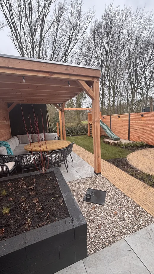 Loungetuin met houten overkapping en sfeervolle beplanting in Rijswijk