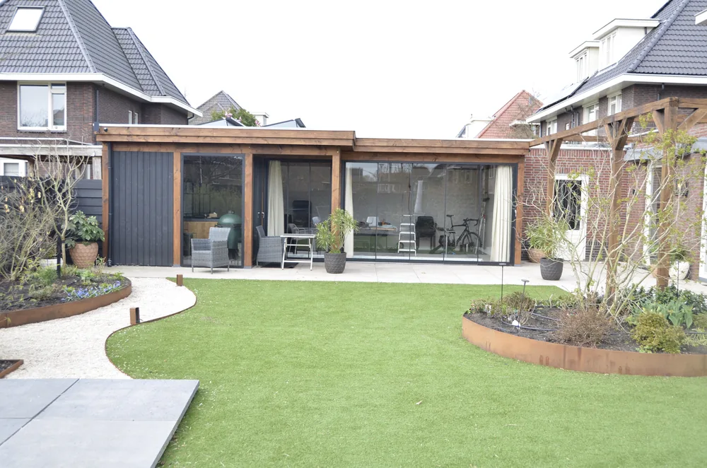 Moderne achtertuin met houten veranda, gebogen gazon en beplanting in Berkel en Rodenrijs
